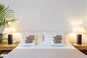 A hotel room with a bed, two nightstands, two lamps, a potted plant, and decorative pillows.