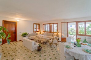 Quarto com sofá, mesa de centro, mesa de jantar posta para dois e uma janela grande com vista para o verde.