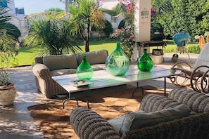 An outdoor seating area with wicker furniture, a glass-top table, and green glass vases.