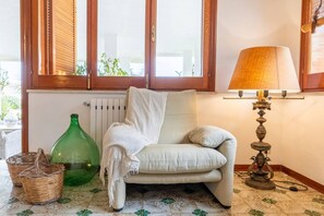 Une pièce avec une fenêtre, un radiateur, une bouteille verte, une lampe et un canapé.