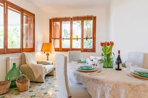 A dining area with a table set for four, a sofa, a lamp, and a vase with flowers.