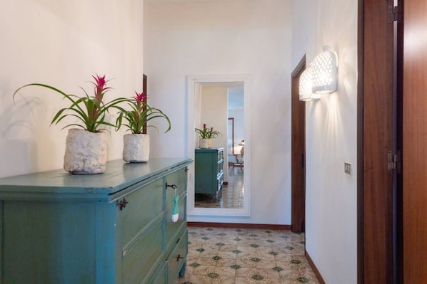 A hallway with a teal dresser, potted plants, a mirror, and a wall-mounted light fixture.