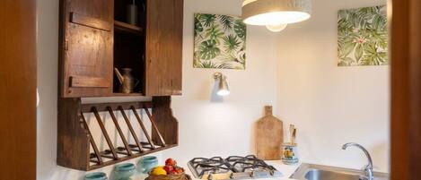 A kitchen with a gas stove, wooden cabinets, a hanging light fixture, and a sink.