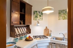A kitchen with a gas stove, wooden cabinets, a hanging light fixture, and a sink.