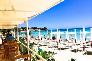A beachside restaurant with outdoor seating overlooking a pool and beach.