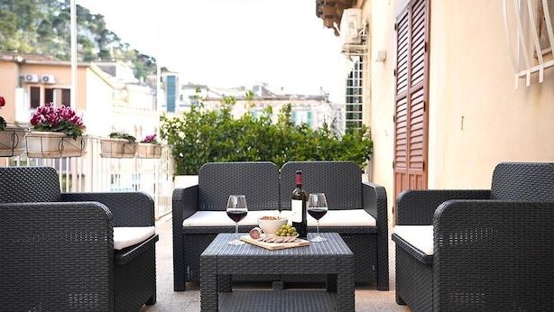 An outdoor seating area with wicker furniture, a table with a bottle of wine, glasses, and a bowl of snacks.