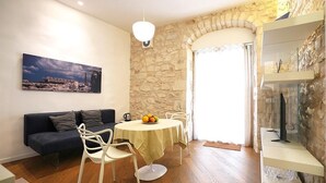 A dining area with a round table, white chairs, a blue sofa, and a stone wall.