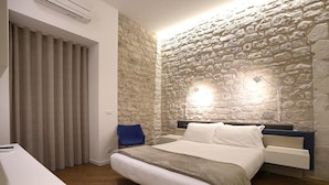 A bedroom with a stone wall, a bed with white bedding, a bedside table, and a chair.