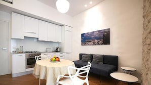 A compact kitchen with white cabinets, a dining table with chairs, a sofa, and a small table.