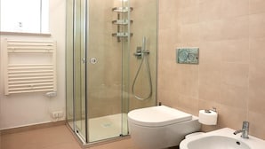 A modern bathroom with a glass-enclosed shower, a toilet, and a bidet.