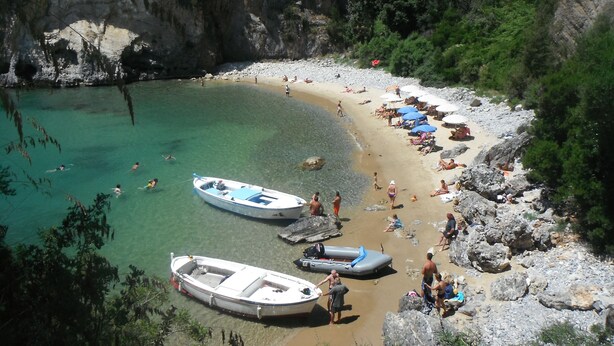 Une plage avec des bateaux, des gens et des falaises rocheuses.