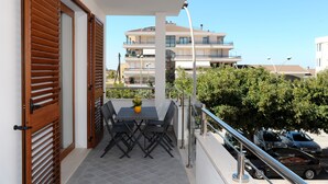 A balcony with a table and chairs, a potted plant, and a view of a multi-story building. - ALKIRA LODGE - ILUKA Two-bedroom apartment with sea view (Alghero)