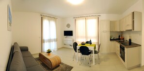 Un ambiente compatto con divano, tavolo da pranzo, sedie, televisione e angolo cottura.