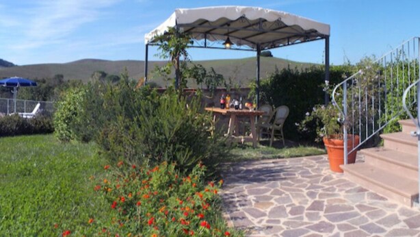 A pool area with lounge chairs and umbrellas, a covered patio with a table and chairs, and a stone pathway leading to a staircase. - Apartment Rosa 4 + 1 (Lajatico)