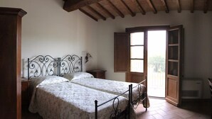 A bedroom with a double bed, wooden ceiling beams, a window with a view, and a small bedside table. - Apartment Rosa 4 + 1 (Lajatico)