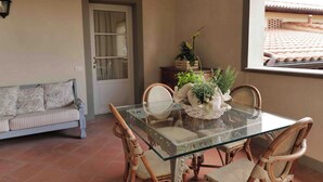 A dining area with a glass table surrounded by wicker chairs, a cushioned sofa, and a potted plant on a tiled floor. - AGRITURISMO IL PRINCIPINO Apartment 6 (San Donato)