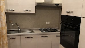 A kitchen with white cabinets, a stainless steel sink, a gas stove, and a black oven. - AGRITURISMO IL PRINCIPINO Apartment 6 (San Donato)