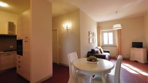 A compact kitchen with a dining area, a television, and a window with curtains. - AGRITURISMO IL PRINCIPINO Apartment 6 (San Donato)