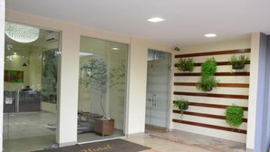 A hotel reception area with a modern design, featuring a glass door entrance, a wooden panel wall with greenery, and a 'Reguinte Hotel' doormat. - Requinte Hotel (Altamira)