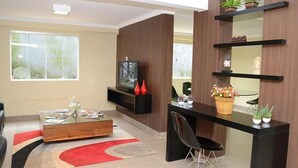 A modern living room with a TV, a coffee table, and a dining area with a black chair. - Requinte Hotel (Altamira)