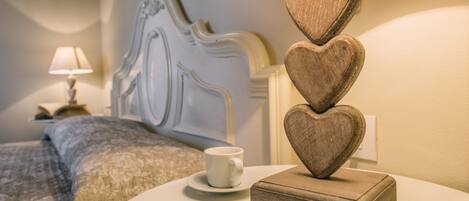 Habitación de hotel ordenada con cama, mesita de noche con lámpara, taza y un objeto decorativo con forma de corazón.