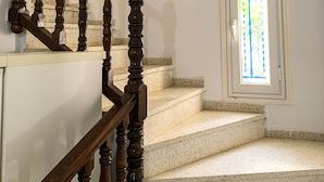 A staircase with wooden balusters leading to a landing, a small window with a metal grille, and a speckled floor. - House with garden in a residential area 100 m from a magnificent beach (Unknown)