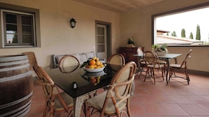 A dining area with a glass table, wicker chairs, a wooden barrel, and a bowl of fruit. - FARM THE PRINCIPIN Apartment 5  (Vinci FI)