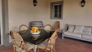 A dining area with a glass table surrounded by wicker chairs, a bowl of fruit, and a striped sofa against a wall with two wall-mounted lamps. - FARM THE PRINCIPIN Apartment 5  (Vinci FI)