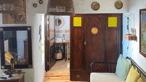 A room with exposed wooden beams, a bed with striped bedding, a green patterned rug, a wooden wardrobe, and a mirror with a decorative item on the dresser. - MILL HOUSE 1 - HOLIDAY HOUSE (Santa Cruz - Torres Vedras)