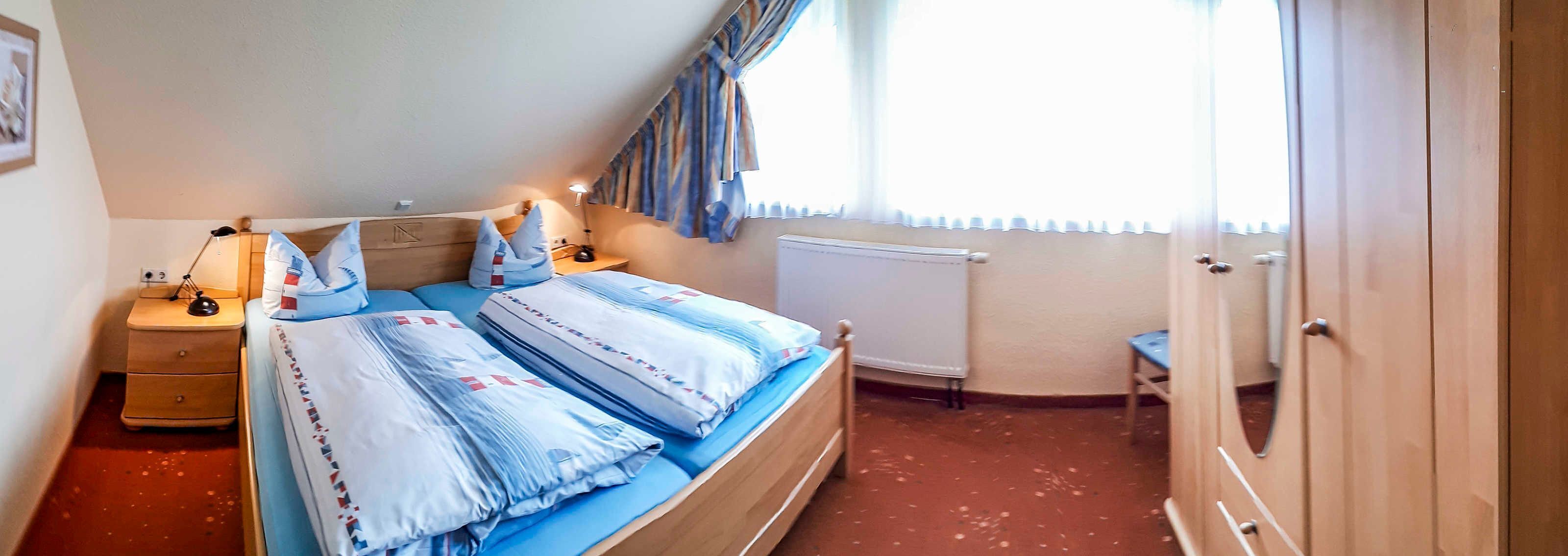 A bedroom with a bed, bedside tables, a lamp, a radiator, and a window with curtains.