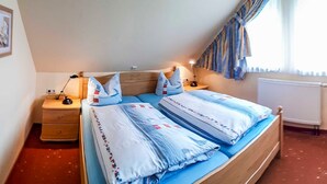 A bedroom with a bed, bedside tables, a lamp, a radiator, and a window with curtains. - Apartment 16 - apartment / apartment in Binz (Binz)