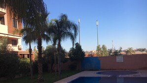 A swimming pool with a tiled deck, surrounded by palm trees and a building with an air conditioning unit.