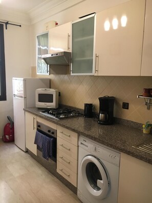 Cocina compacta equipada con estufa a gas, microondas, cafetera y lavadora.