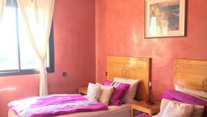 A hotel room with two beds, each with pink and white bedding, a wooden headboard, and a painting on the wall.