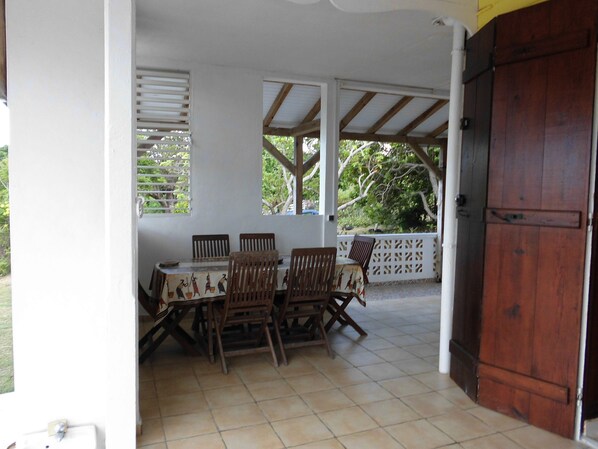 Un área de patio techada con una mesa y sillas, una puerta de madera y vistas a la vegetación.