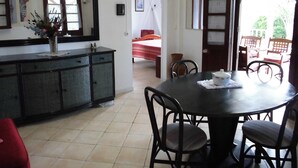 Un coin repas avec une table ronde et des chaises, un petit meuble avec un miroir, et un lit à l’arrière-plan.