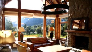 A cozy living room with a stone fireplace, wooden furniture, and large windows offering a scenic mountain view.