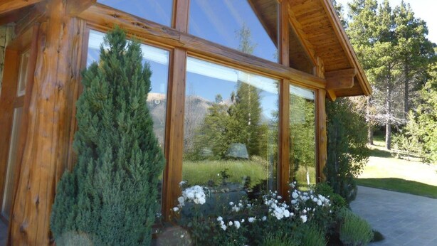 A wooden cabin with large windows reflecting a mountainous landscape.