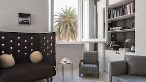 Un salon moderne avec un canapé foncé, un fauteuil gris, une petite table d’appoint sur laquelle se trouve une théière, et une bibliothèque remplie de livres.