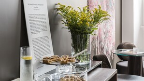Une table avec un pichet en verre, un verre d’eau, un vase de fleurs jaunes, un bocal en verre rempli de biscuits et une pancarte avec du texte.