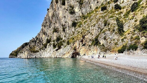 Ein klares, flaches Küstengebiet mit einer felsigen Klippe und einem Kiesstrand.