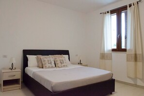 Un dormitorio con una cama, dos mesitas de noche y un ventanal con cortinas.