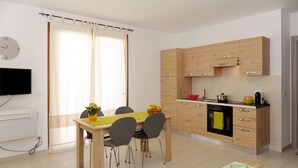 A modern kitchen with wooden cabinets, a dining table with chairs, and a television mounted on the wall. - ALKIRA LODGE - Residential Hotel Apartments (Alghero)