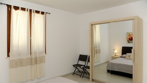 A bedroom with a bed, a chair, a nightstand, a lamp, and a large mirror. - ALKIRA LODGE - Residential Hotel Apartments (Alghero)