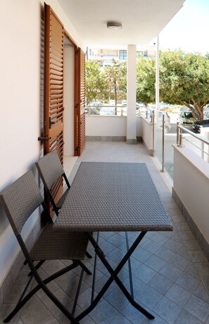 Un balcon avec une table et des chaises, une porte en bois et une vue sur la rue et les arbres.