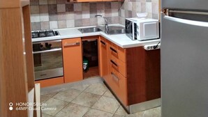 Eine kleine Küche mit orangefarbenen Schränken, einem Edelstahlkühlschrank, einer Mikrowelle und einem Gasherd.