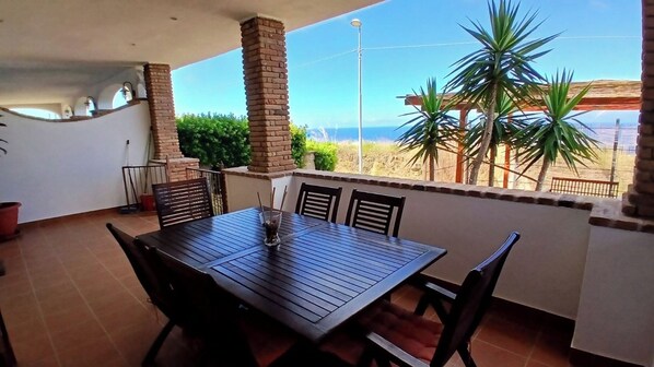 An outdoor patio with a table and chairs, a brick column, and a view of the ocean.