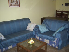 Ein Wohnzimmer mit einem blauen Sofa, einem Glastisch und einem kleinen dekorativen Gegenstand auf dem Tisch.