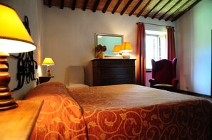 Ein Hotelzimmer mit einem Bett, zwei Nachttischlampen, einem Schminktisch mit Spiegel, einem Sessel und einem Fenster mit Vorhängen.
