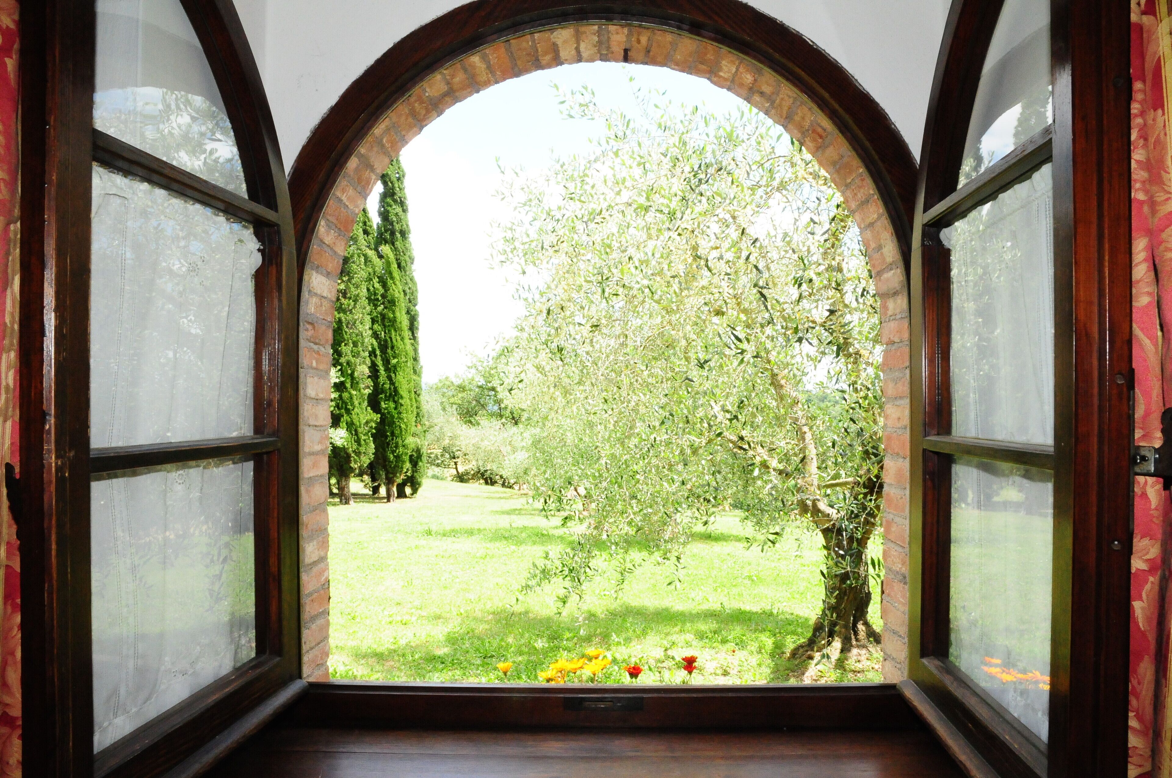 Ein Zimmer mit einem Rundbogenfenster mit Blick auf einen Garten mit Bäumen und Blumen.
